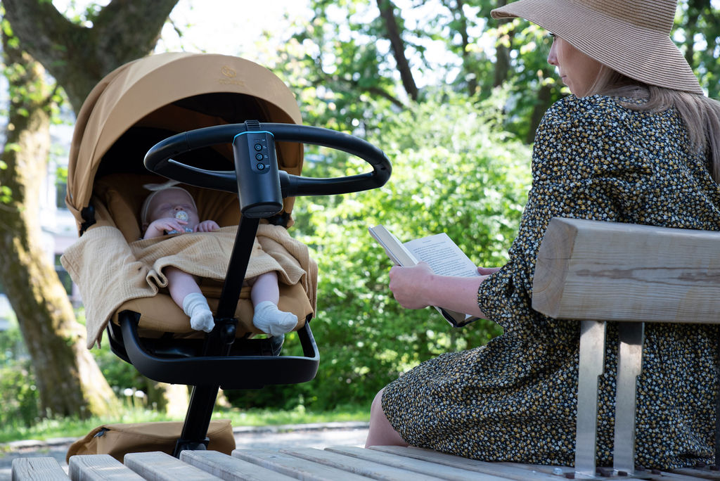 Mum reading on a park bench while her baby sleeps in the stroller