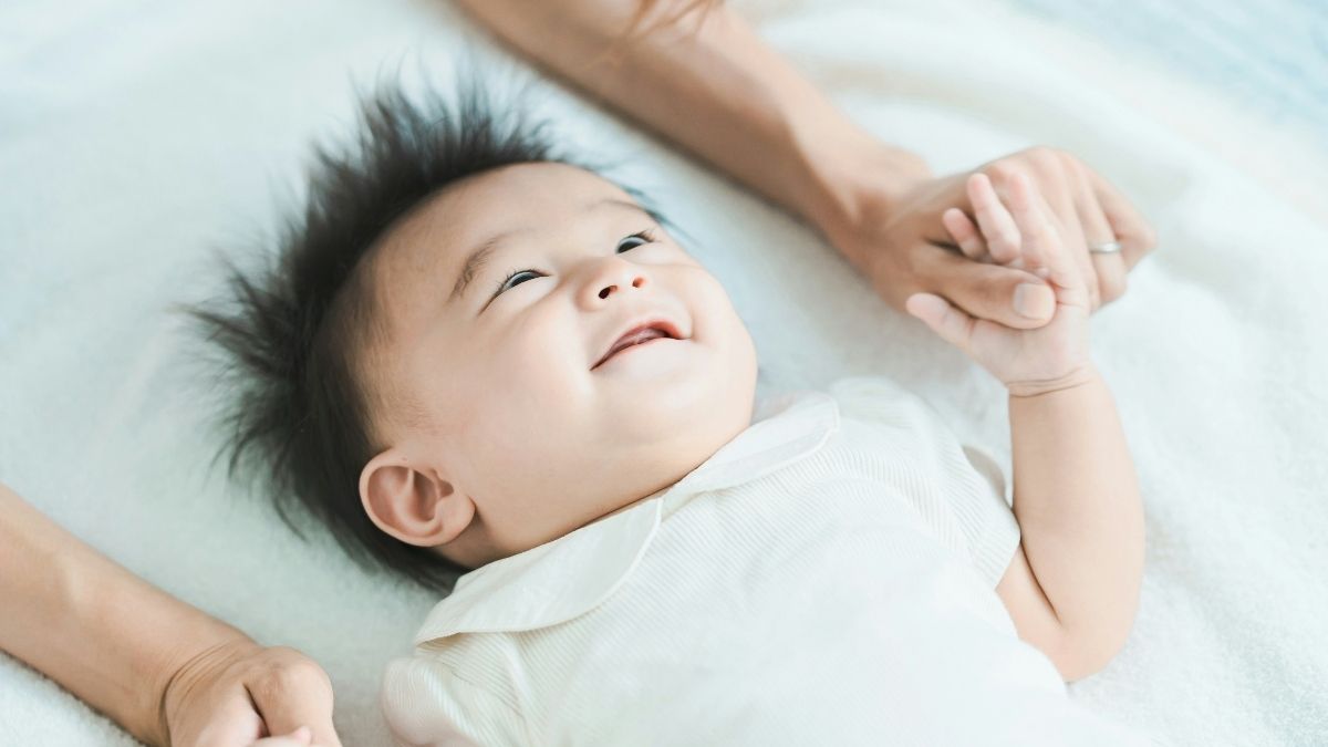 Little boy smiling and holding parents hands in bed