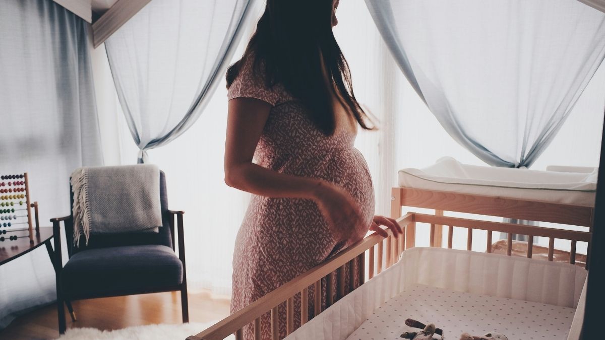 Pregnant woman standing by a wooden crib in a prepared nursery